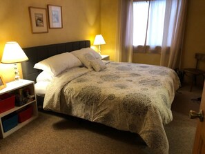 Une chambre d’hôtel comprenant un lit, deux lampes de chevet, une table de chevet avec des compartiments de rangement et une fenêtre avec des rideaux.