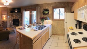A cozy living room with a fireplace, a dining area, and a kitchen with a stove and sink. - Riverfront condo #3 w/patio, 1block 2 town,King bed,Wifi,20 min ski Granby Ranch (GRAND LAKE)