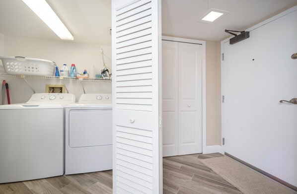 A laundry area with two washing machines and a drying rack, a white door, and a ceiling-mounted projector. - Gorgeous 3/3 Oceanfront at Seychelles -- Unit 504 (Daytona Beach Shores)