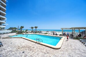 A swimming pool with a view of the beach, lounge chairs, and a covered area.