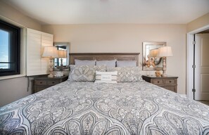Quarto com uma cama grande, duas mesas de cabeceira, uma cabeceira e uma mesinha de apoio com luminária.