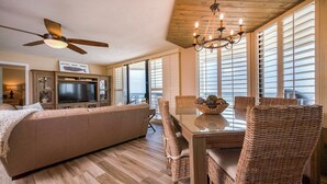 A spacious living area with a large sofa, a dining table with wicker chairs, a ceiling fan, and a chandelier. - Gorgeous 3/3 Oceanfront at Seychelles -- Unit 504 (Daytona Beach Shores)