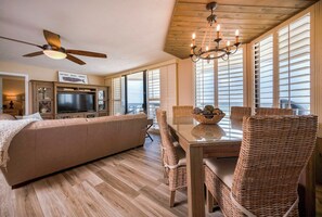 A spacious living area with a large sofa, a dining table with wicker chairs, a ceiling fan, and a chandelier. - Gorgeous 3/3 Oceanfront at Seychelles -- Unit 504 (Daytona Beach Shores)