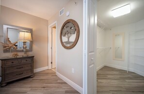 A hallway with a wooden dresser, a mirror, and a wall-mounted tree decoration. - Gorgeous 3/3 Oceanfront at Seychelles -- Unit 504 (Daytona Beach Shores)