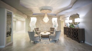 A modern interior with a round table and four chairs, a decorative chandelier, and a stone wall. - Gorgeous 3/3 Oceanfront at Seychelles -- Unit 504 (Daytona Beach Shores)