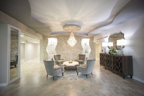 A modern interior with a round table and four chairs, a decorative chandelier, and a stone wall. - Gorgeous 3/3 Oceanfront at Seychelles -- Unit 504 (Daytona Beach Shores)