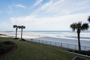 A beach view with a fence, palm trees, and a clear sky.