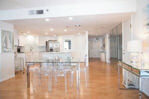Cozinha moderna com armários brancos, uma ilha central e área de jantar com cadeiras transparentes.