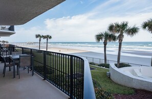 Ein Balkon mit Blick auf den Strand, Palmen und einer Sitzgelegenheit mit Stühlen und Tisch.