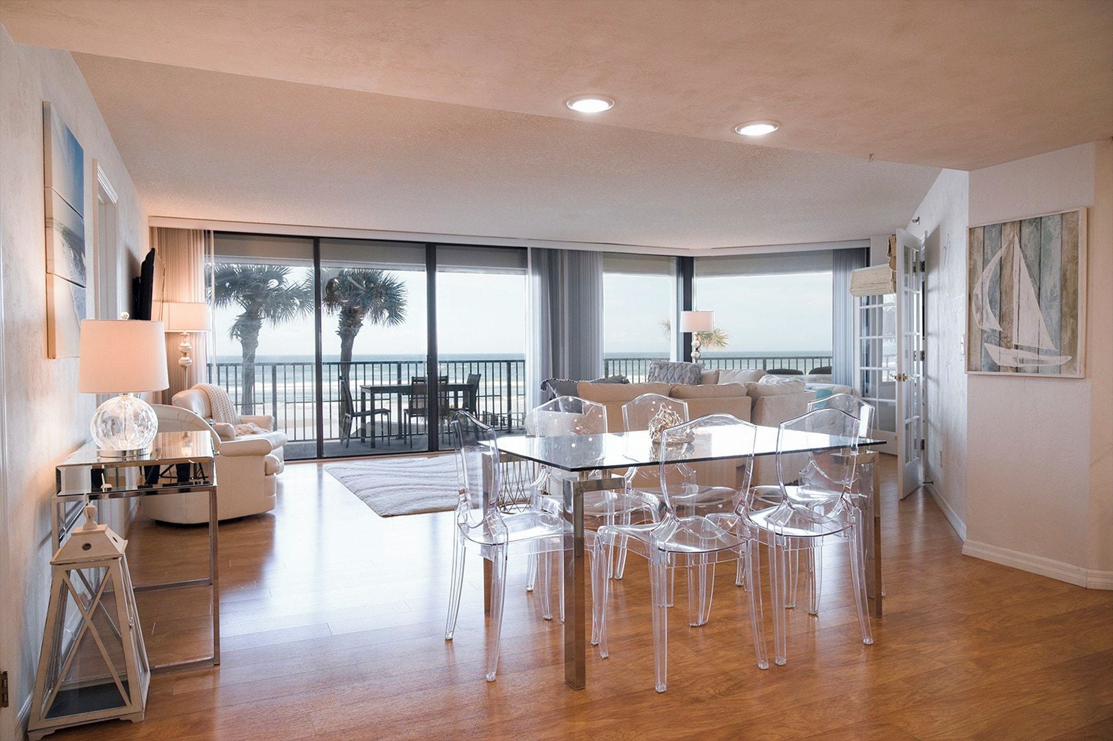 A spacious living area with a glass dining table, clear chairs, and a view of the beach.