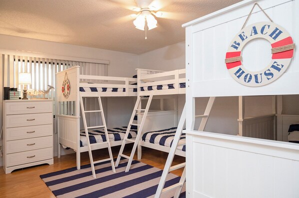 A bunk bed room with a ladder, a dresser, a striped rug, and a wall decoration.