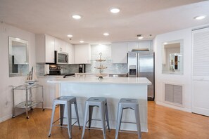 A modern kitchen with a central island, stainless steel appliances, and a glass display cabinet.