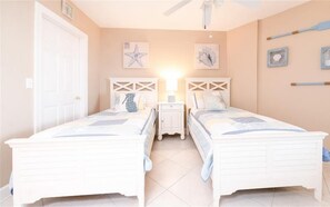 Een slaapkamer met twee bedden, een nachtkastje en een plafondventilator.