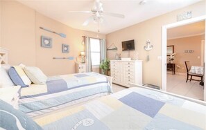 Un dormitorio con dos camas, ventilador de techo, televisión y cómoda.