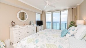 Une chambre dotée d’un grand lit, d’un ventilateur de plafond, d’une télévision, d’une commode et d’un balcon offrant une vue sur l’océan.