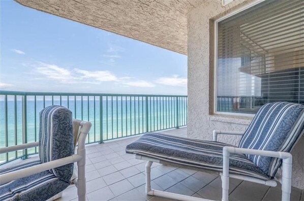 Een balkon met twee gestreepte loungestoelen, uitzicht op de oceaan en een raam met zonwering.