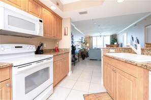 A modern kitchen with white appliances, wooden cabinets, and a tiled floor. - Beautiful Oceanfront 2/2 Condo at Dimucci Twin Towers Unit 1207 (Daytona Beach Shores)