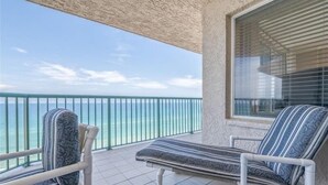 Un balcon avec deux fauteuils de jardin à rayures, une vue sur l’océan et une fenêtre avec des stores.