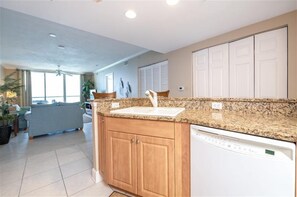 A kitchen with granite countertops, wooden cabinets, a dishwasher, and a window with blinds. - Beautiful Oceanfront 2/2 Condo at Dimucci Twin Towers Unit 1207 (Daytona Beach Shores)