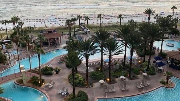 Ett poolområde på ett semesterhotell med flera pooler, palmer och en strand i bakgrunden.