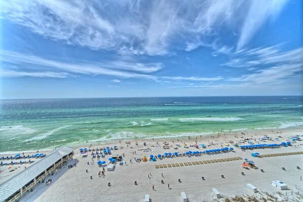 A beach with a wide sandy area, a pier with umbrellas, and the ocean in the background.