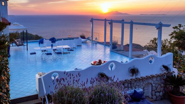 Zona de piscina en la azotea con vista al atardecer, mobiliario exterior y una torre de campanas.