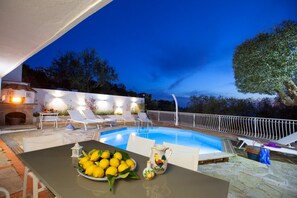 Zona de piscina exterior con sillas de descanso, una mesa con limones y una chimenea.