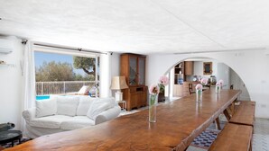 Amplia sala de estar con una larga mesa de madera, sofá blanco y vistas al exterior.