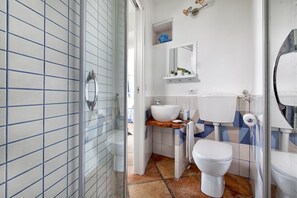 Un baño con cabina de ducha de vidrio, un lavamanos blanco con encimera de madera, inodoro blanco y piso con baldosas azules y blancas.