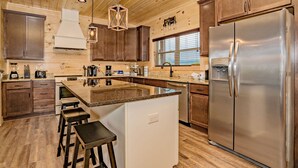 A modern kitchen with wooden cabinets, a stainless steel refrigerator, and a central island with stools. - 11 Miles to Gatlinburg! Indoor Heated Pool/Theater Room/Hot Tub/ DISCOUNTS! (Sevierville)