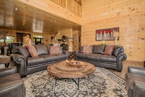 A spacious living room with a large wooden ceiling, two leather sofas with patterned cushions, a round coffee table, and a patterned rug.