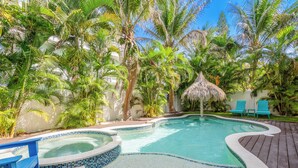 A swimming pool with a tiled edge, surrounded by palm trees and a wooden deck. - EV Charger, Portside Paradise by SeaBreeze Vacation (Holmes Beach)