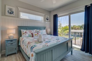 A bedroom with a bed, a nightstand, a window with blinds, and a view of the outdoors. - Portside Paradise (Holmes Beach)