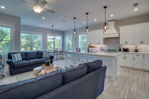 A modern kitchen with white cabinets, a central island, pendant lighting, and a dining area with a sofa and chairs. - Portside Paradise (Holmes Beach)