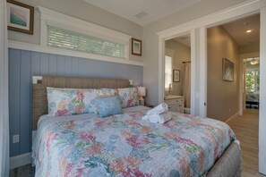 A bedroom with a large bed, a nightstand, a dresser, and a window with blinds. - Portside Paradise (Holmes Beach)