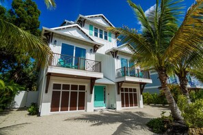 A two-story house with a balcony, a garage, and a palm tree in the foreground.