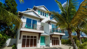 A two-story house with a garage, a balcony, and a tropical garden. - EV Charger, Portside Paradise by SeaBreeze Vacation (Holmes Beach)