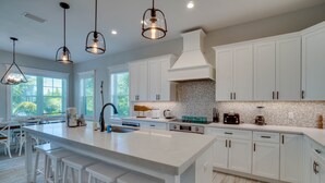 A spacious kitchen with a large island, white cabinetry, and pendant lighting. - EV Charger, Portside Paradise by SeaBreeze Vacation (Holmes Beach)