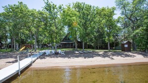 A lakeside park with a sandy beach, a wooden deck, and several lounge chairs.