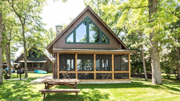 A cabin with a large glass front, wooden deck, and picnic table.