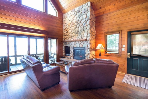 A log cabin interior with a stone fireplace, leather sofas, and large windows. - Waterfront Cabin on Gull Lake w/ Boat Rentals (Nisswa)