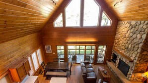 A cozy cabin interior with a stone fireplace, wooden walls, and a dining area.