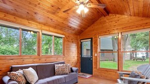 Een houten cabin met een bank, een stoel en een plafondventilator.