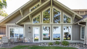 Une maison avec des fondations en pierre, de grandes fenêtres et un patio aménagé avec du mobilier d’extérieur.