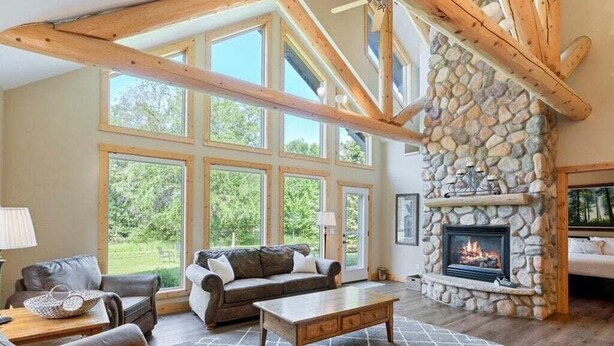 Un salón amplio con chimenea de piedra, ventanas grandes y un techo alto con vigas a la vista.