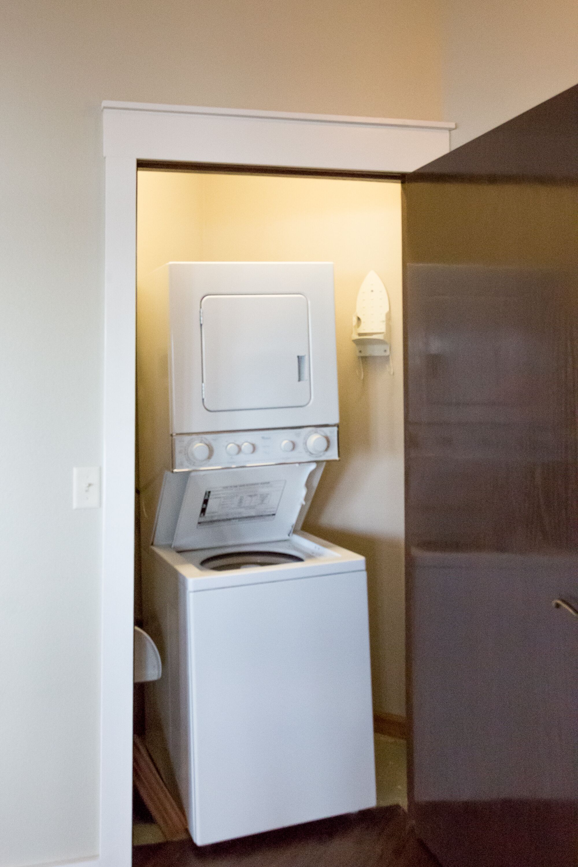 A compact laundry room with a stacked washer and dryer, a small window, and a door leading to another room.