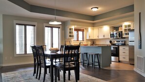 A modern kitchen with a dining area, featuring a central island, dark wooden chairs, and a patterned rug. - Gull Lake at Your Doorstep |Waterfront Rental | Sleep 8 (Nisswa)