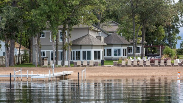 A waterfront property with a dock, lounge chairs, and a building with large windows. - Gull Lake at Your Doorstep |Waterfront Rental | Sleep 8 (Nisswa)