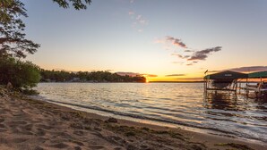Una playa con un atardecer, agua tranquila y un muelle con zona cubierta.