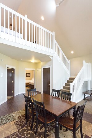 A dining area with a wooden table and chairs, a patterned rug, and a staircase with white railings leading to an upper level.